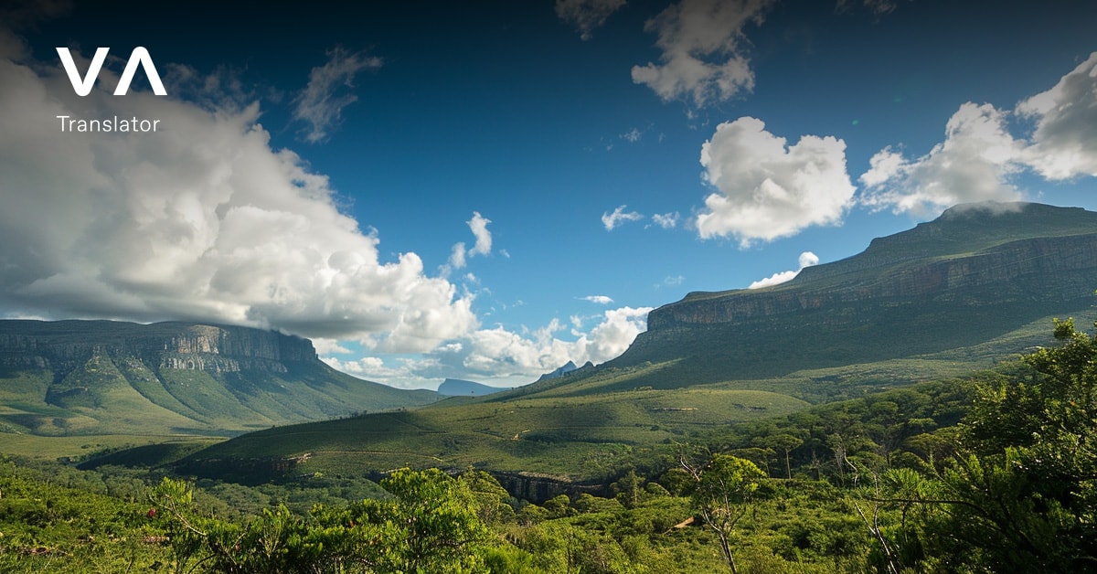 Un vasto paisaje verde con colinas onduladas y montañas bajo un cielo azul con nubes dispersas.