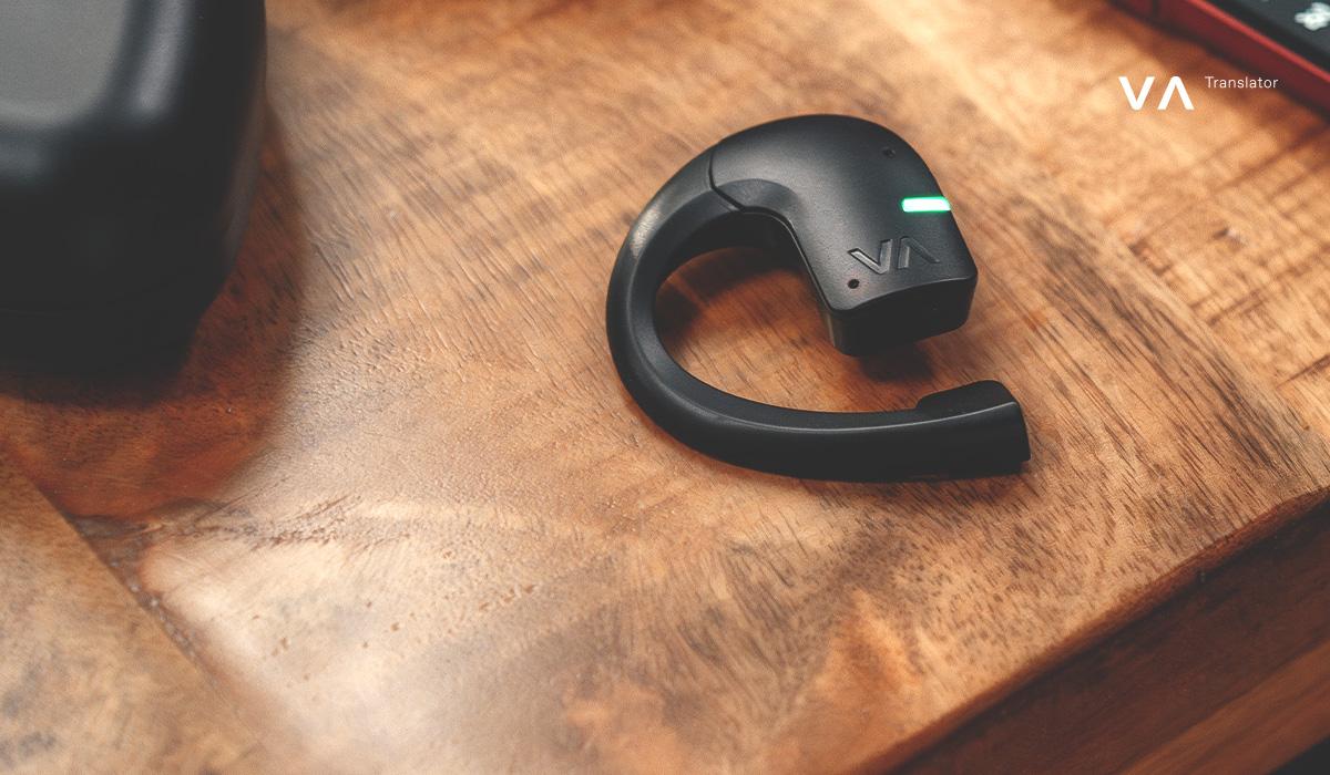 Primer plano de un auricular traductor E1 sobre una mesa de madera con indicador LED.