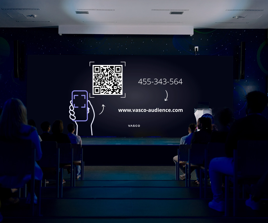 Una gran pantalla situada en la sala de conferencias muestra las instrucciones «Únete a Vasco Audience», con indicaciones para los participantes sobre cómo acceder a la sesión.
