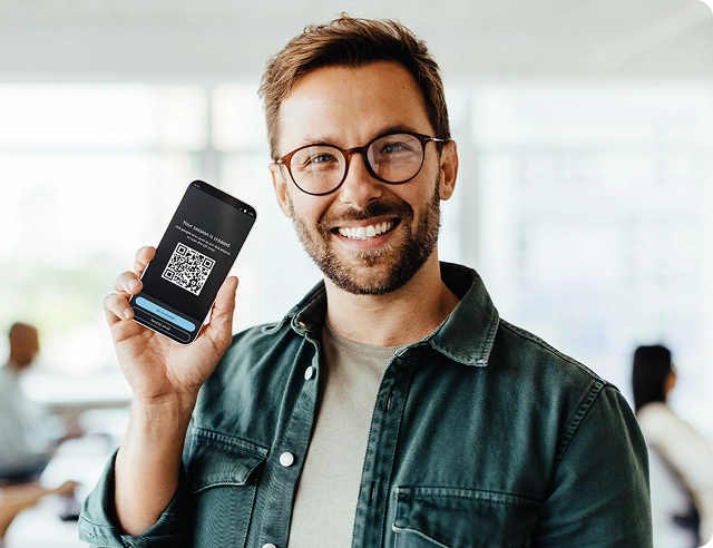 Un hombre sonriente sosteniendo un smartphone en el que se muestra un código QR para unirse a Vasco Audience.