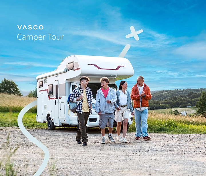 Una familia de cuatro miembros —dos padres y dos hijos— se aleja de su autocaravana aparcada en un día soleado. Sonríen, hablan y disfrutan de la compañía mutua, creando un ambiente cálido y relajado que refleja la alegría de viajar juntos.