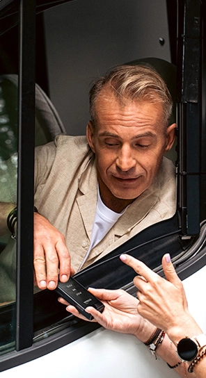 Un hombre sentado en un coche, hablando con el dispositivo Q1 que alguien le está entregando.
