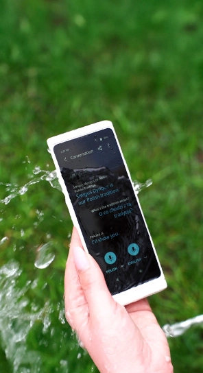 Primer plano de una mano que sostiene el Traductor V4 mientras el agua salpica el dispositivo, lo que pone de relieve su resistencia.