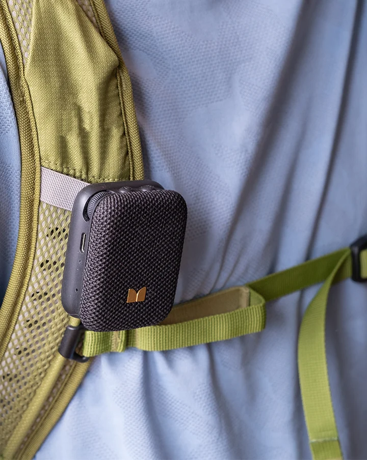 Mini altavoz Bluetooth negro sujeto a la correa verde oliva de una mochila